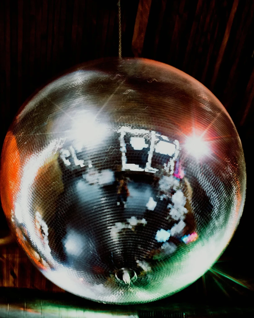 A large disco ball hangs, reflecting starbursts of light in a dark room.