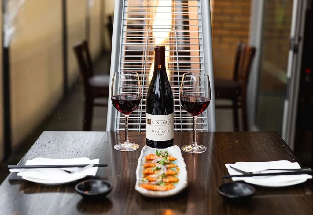 Warmly lit table with Saintsbury Pinot Noir, shrimp, and place settings.