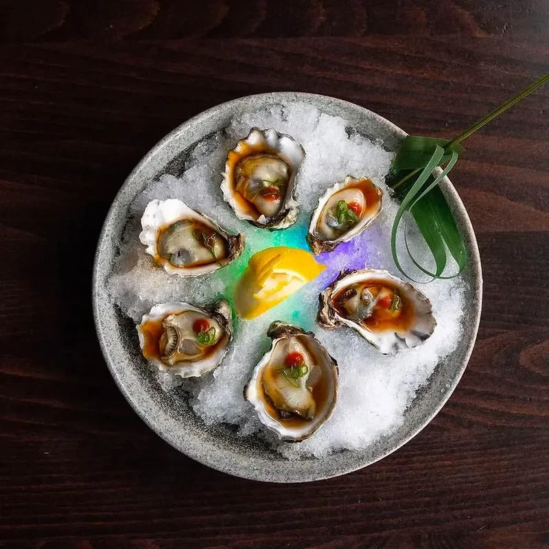 Six oysters with red sauce, green herbs, lemon on glowing ice.