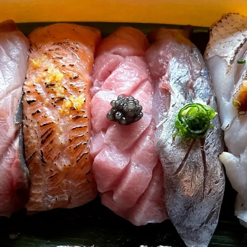 Top-down view of five distinct nigiri sushi and sashimi, side-by-side.