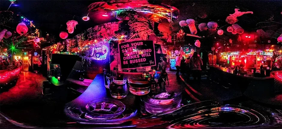 Vibrant, neon-lit nightclub with 'UNATTENDED DRINKS' safety warning sign.