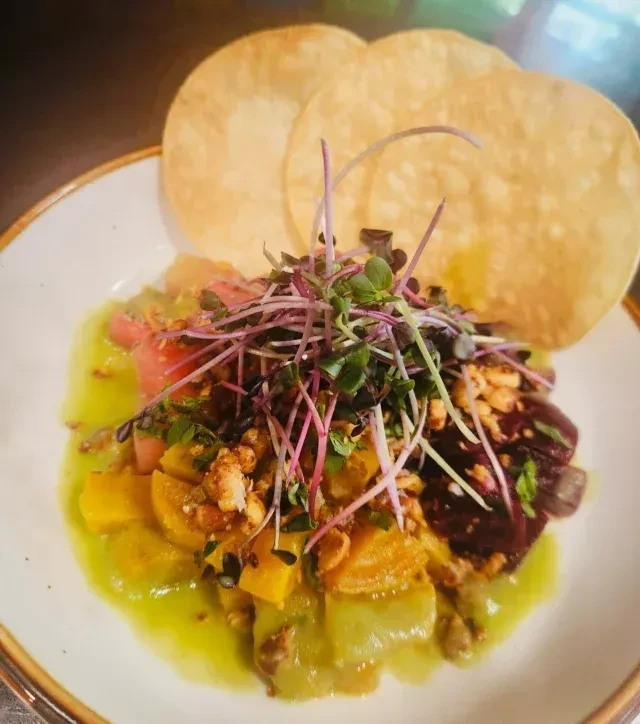 Colorful ceviche or salad in white bowl with microgreens and crisps.