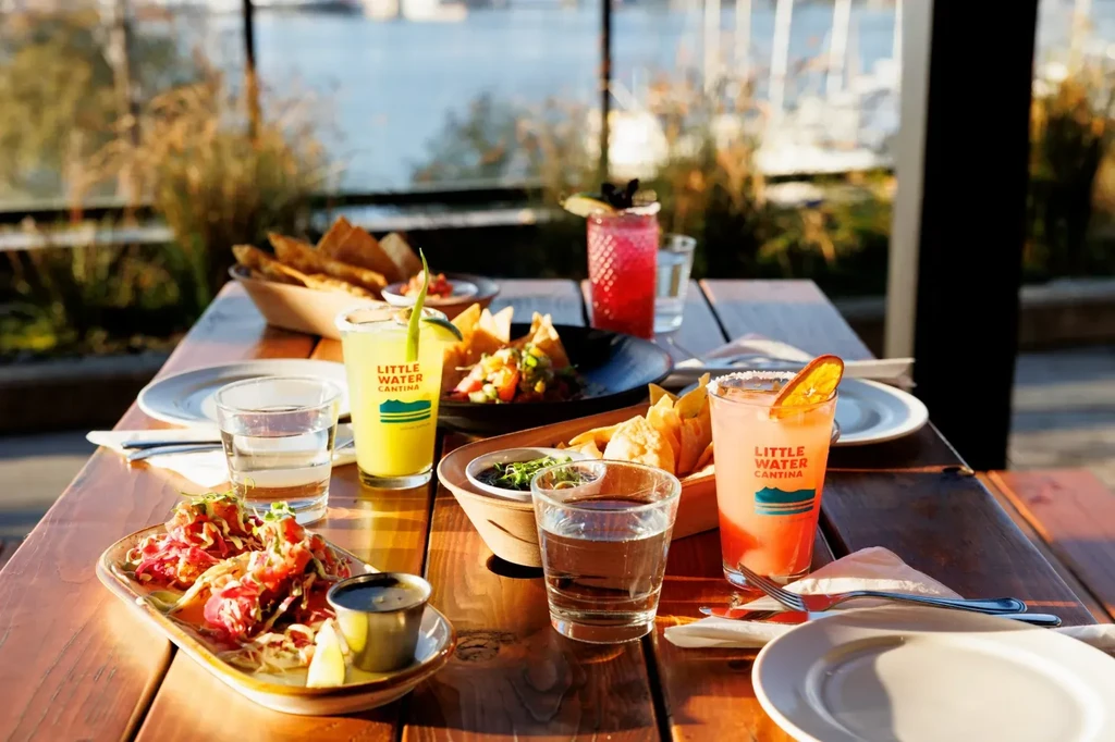 Sunlit outdoor dining table with poke, chips, salad, and Cantina drinks.