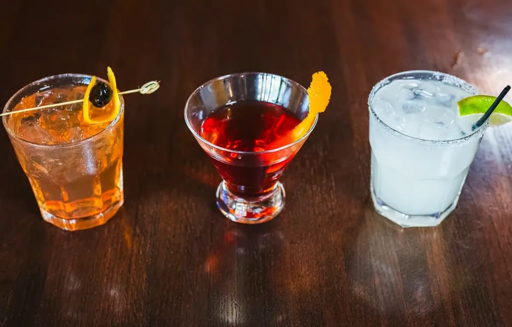 A trio of distinct cocktails on a dark polished wooden surface.