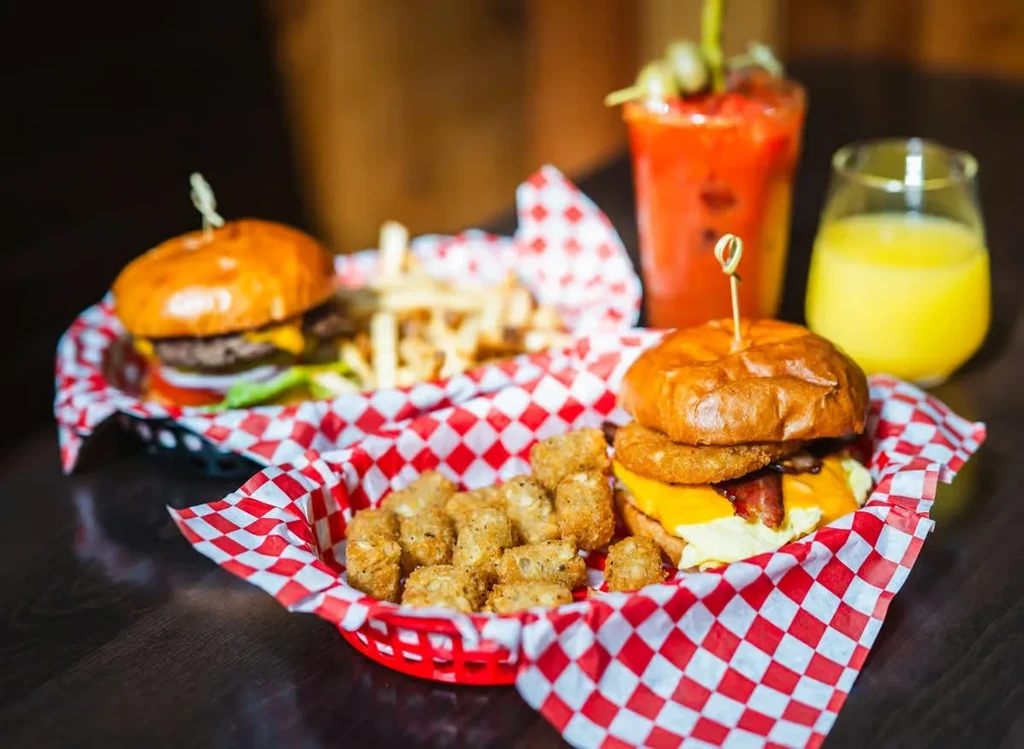 Two burgers, tater tots, fries, a cocktail, and juice.