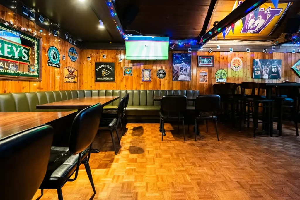 Empty casual restaurant interior featuring booths, tables, sports posters, and string lights.