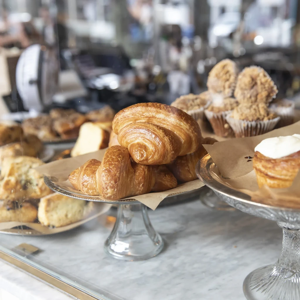 Flaky golden-brown croissants, streusel muffins, and pastries in a bakery display.