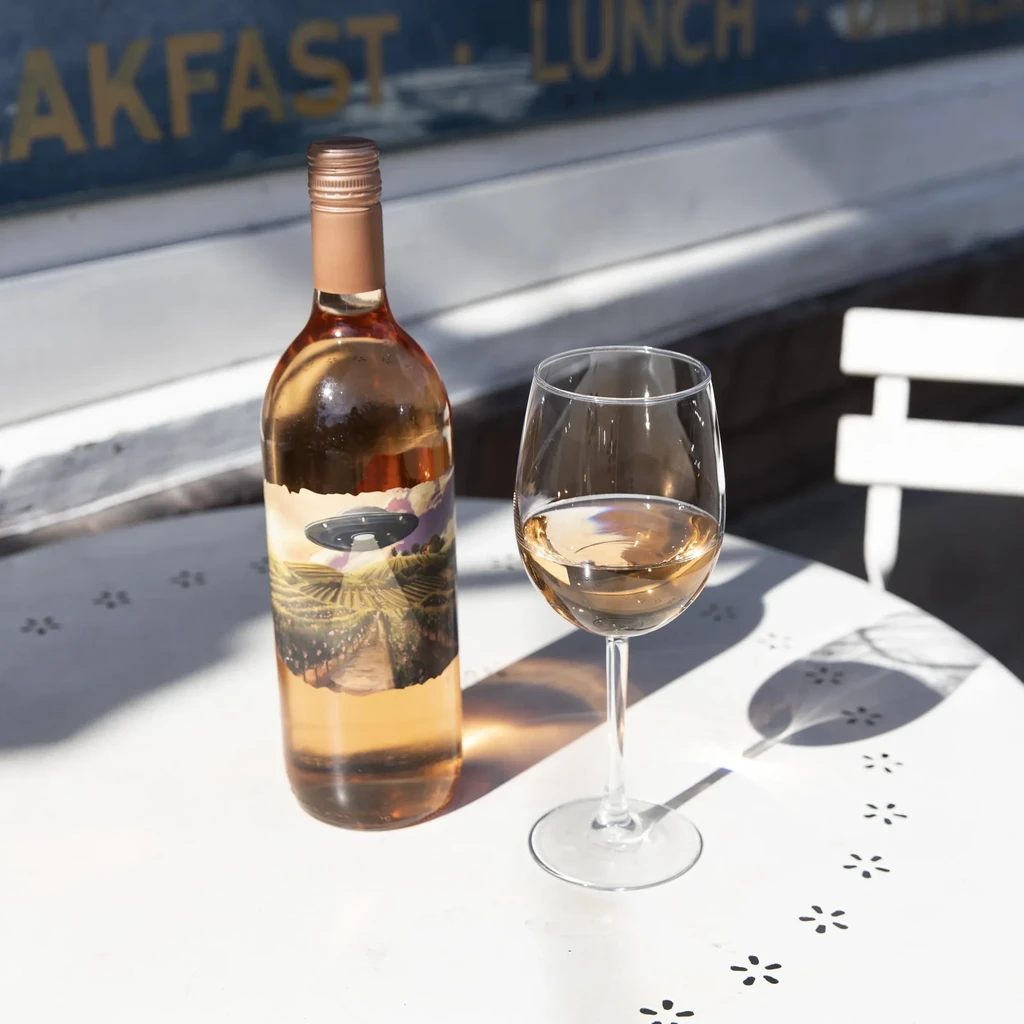 Rosé wine bottle and glass on sunny table with UFO label.