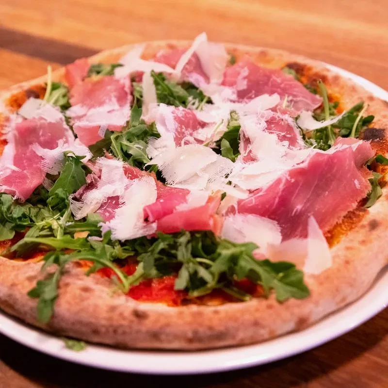 Pizza with blistered crust, tomato sauce, arugula, prosciutto, and Parmesan.