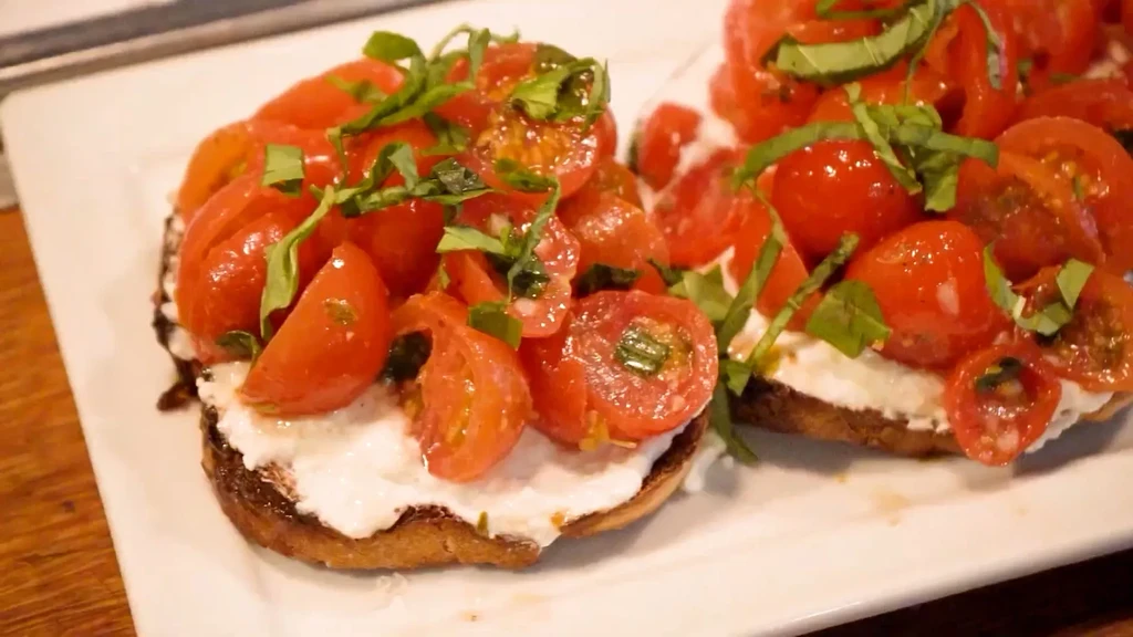 Two bruschetta with creamy cheese, cherry tomatoes, and fresh basil.