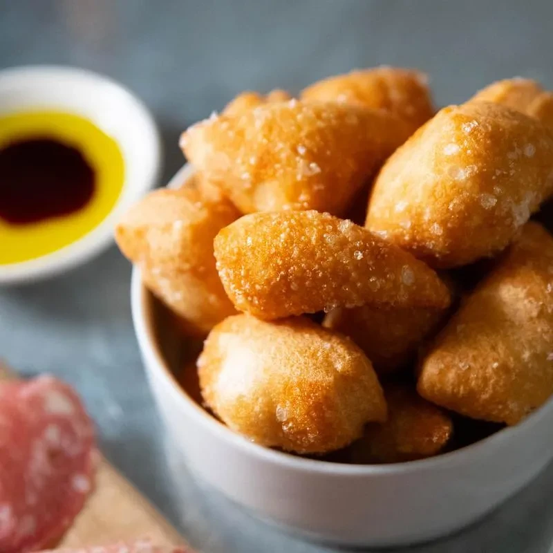 Golden fried dough in a bowl, with dipping sauce and charcuterie.