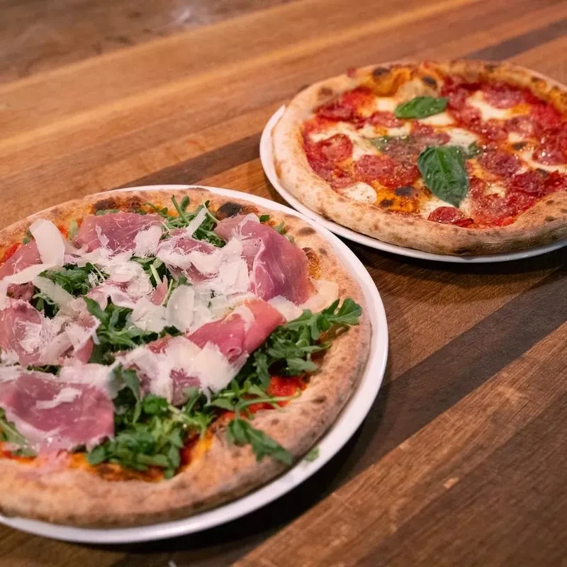 Two pizzas: prosciutto-arugula and pepperoni, on a rustic wooden table.