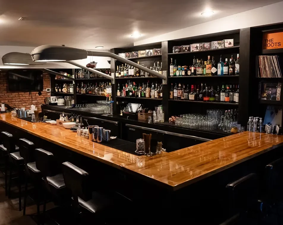 Well-stocked wooden bar interior with liquor bottles, bar stools, vinyl records.