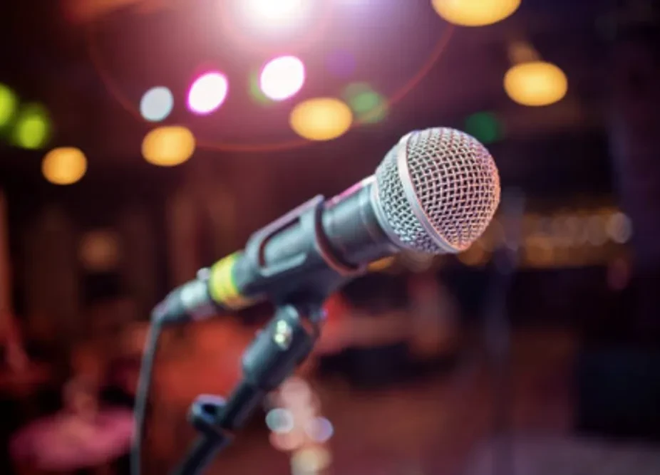 Angled metallic microphone with glowing bokeh stage lights.