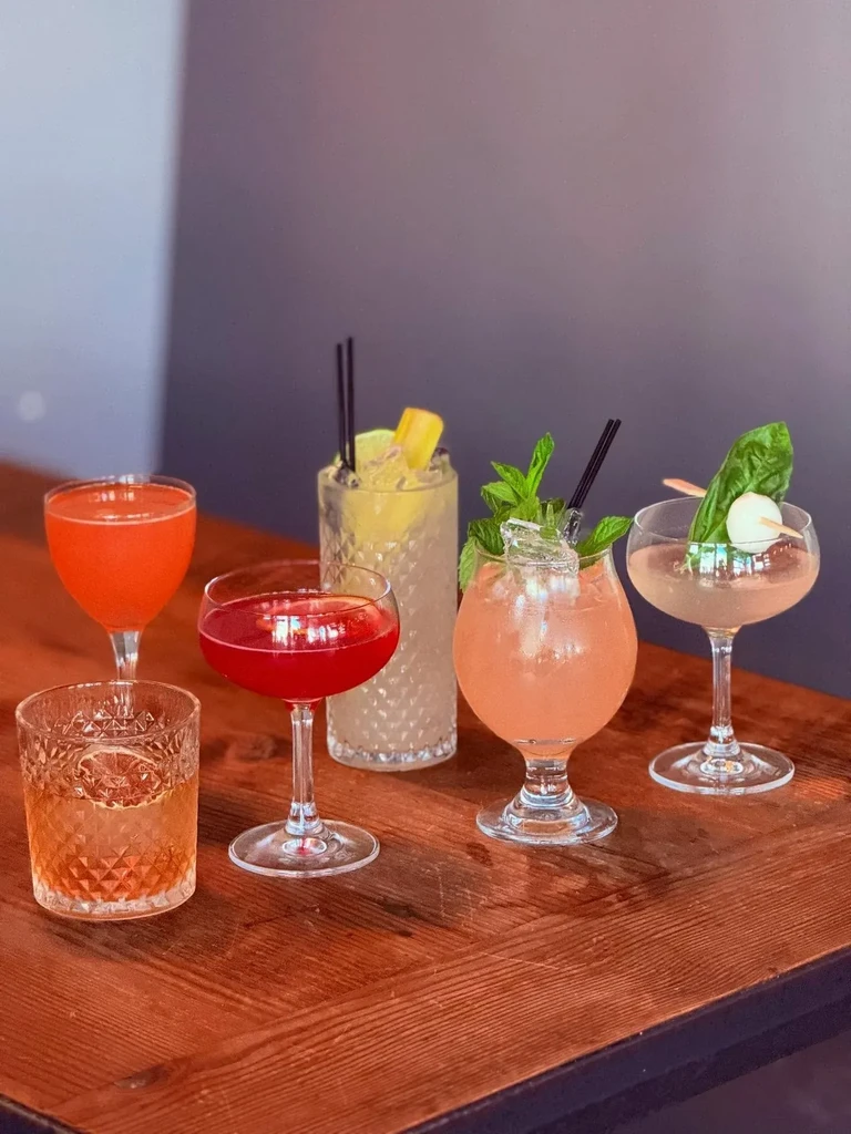 Six diverse cocktails with various garnishes on a wooden table.