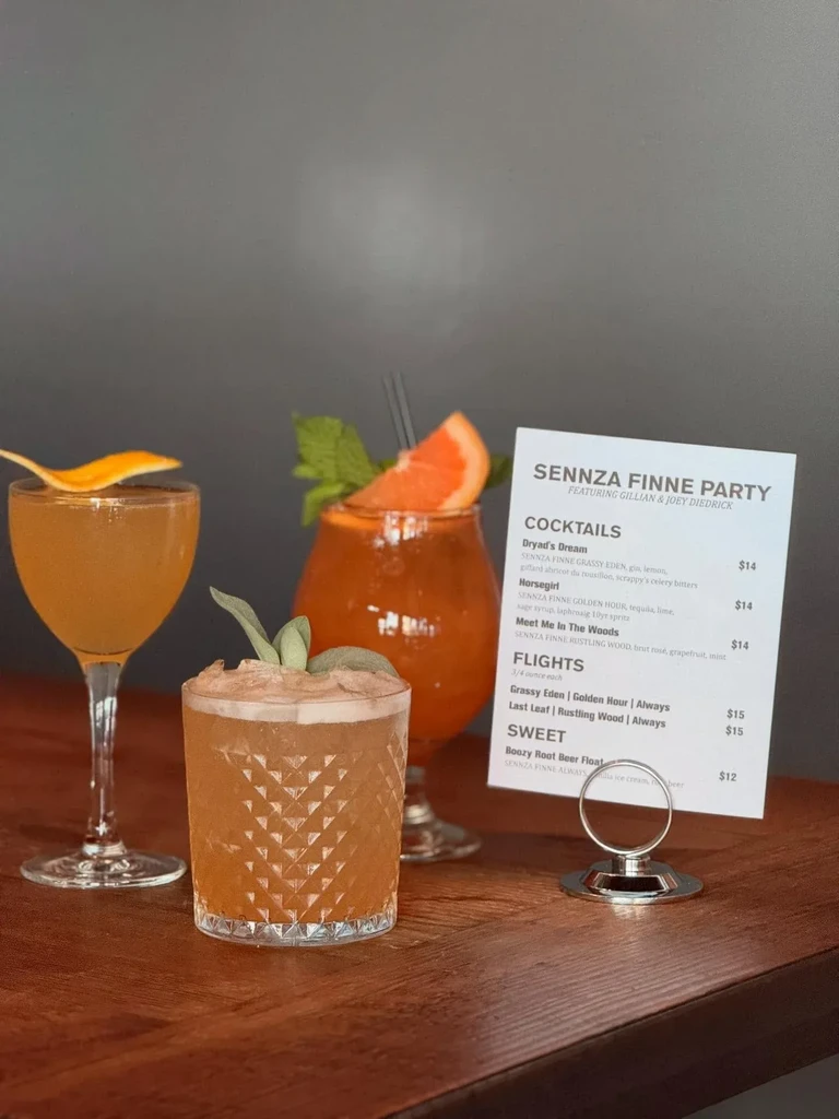 Three amber cocktails with garnishes and a menu on a wooden table.