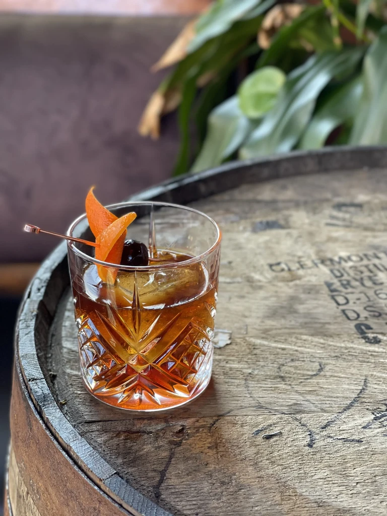Whiskey cocktail with orange and cherry on a distillery rye barrel.
