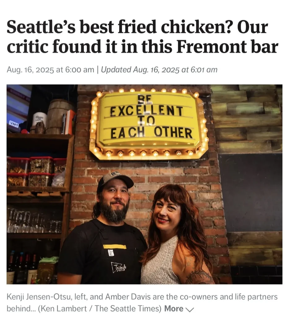 Smiling bar co-owners stand before a 'BE EXCELLENT' marquee sign.