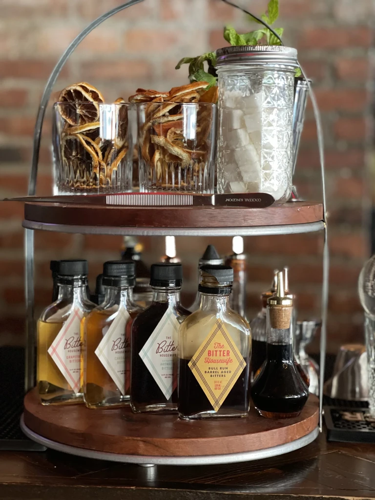 Two-tiered stand with 'The Bitter Housewife' bitters and cocktail garnishes.