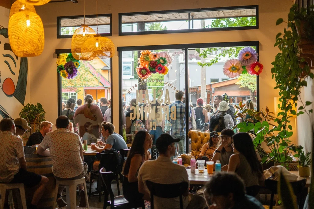 Lively brewery interior with people, warm lights, and decorated windows.