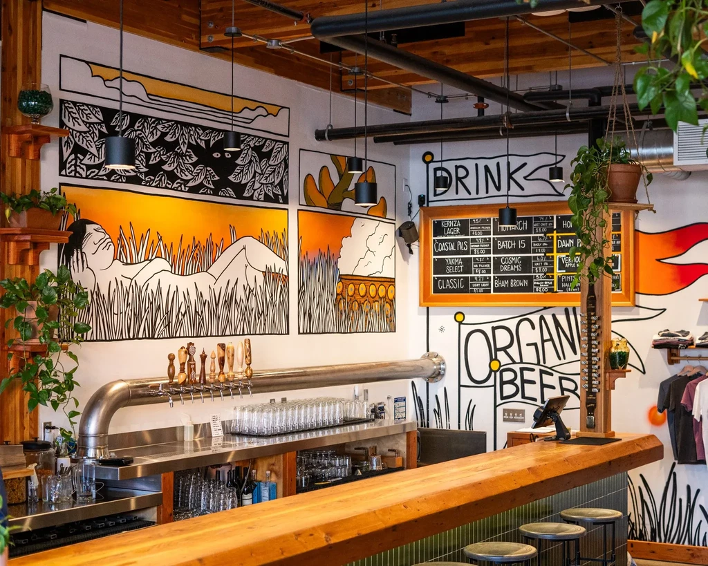 Modern industrial brewery with wooden bar, beer taps, and graphic murals.