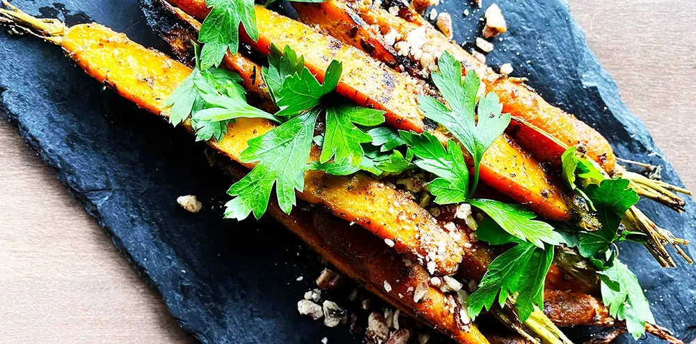 Roasted carrots with parsley and chopped nuts on a slate board.