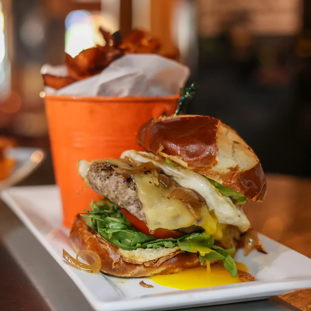 Gourmet burger with runny egg, melted cheese, arugula, pretzel bun.