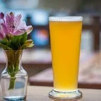 Glass of golden beer and pink, purple alstroemeria flowers on table.