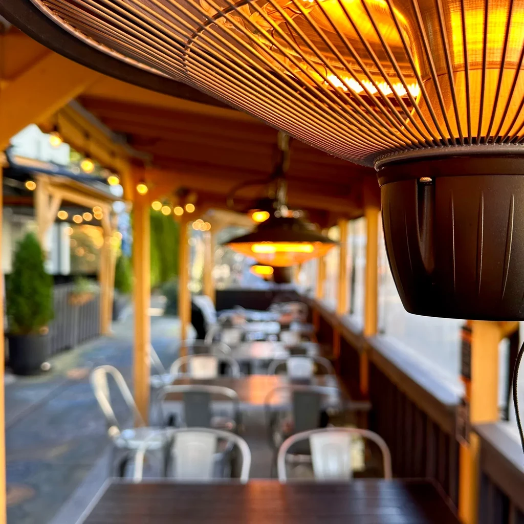 Glowing overhead patio heater warms an empty outdoor dining area.