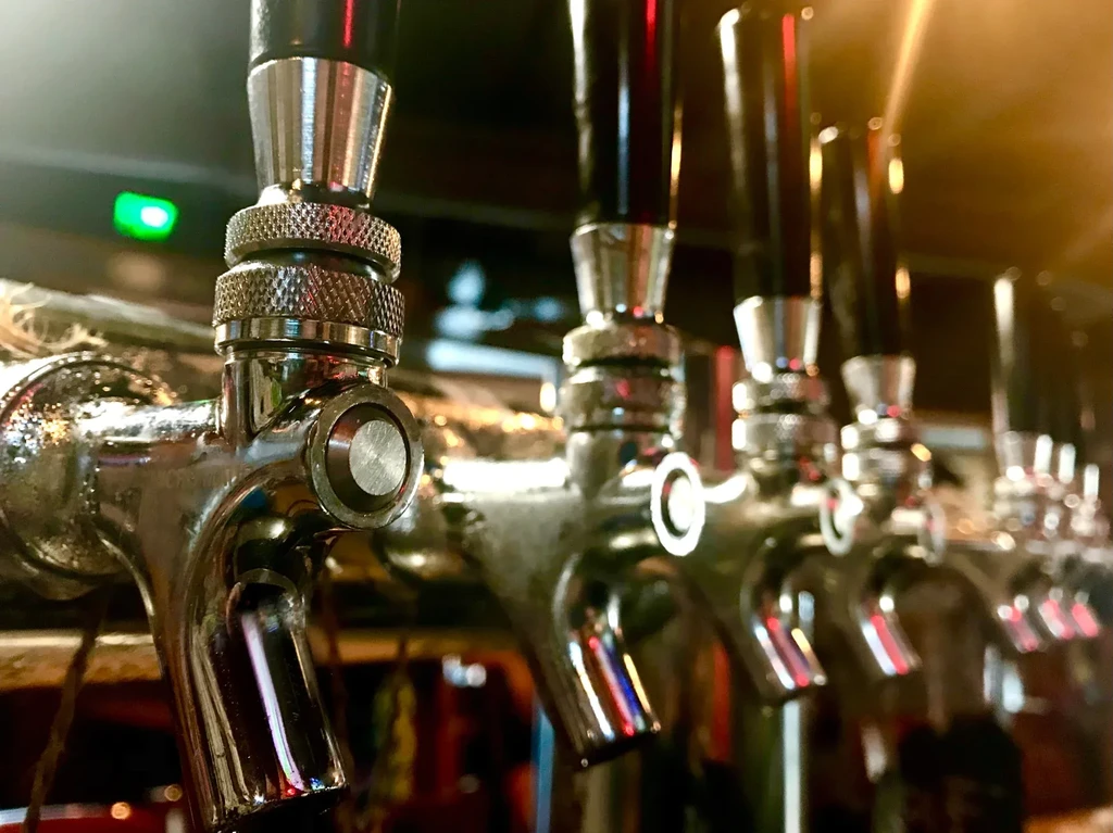 Close-up of a row of polished metallic taps in a dim bar.
