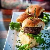 Three sliders, dark patties, green lettuce, on a white plate.