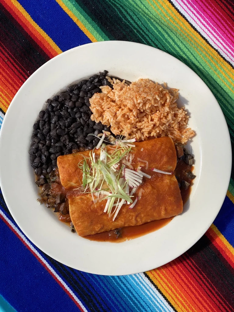 Mexican meal: enchiladas, beans, rice, garnished, on colorful serape.
