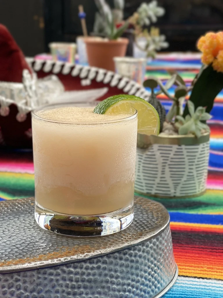 Frosty margarita with lime on metal and colorful serape.