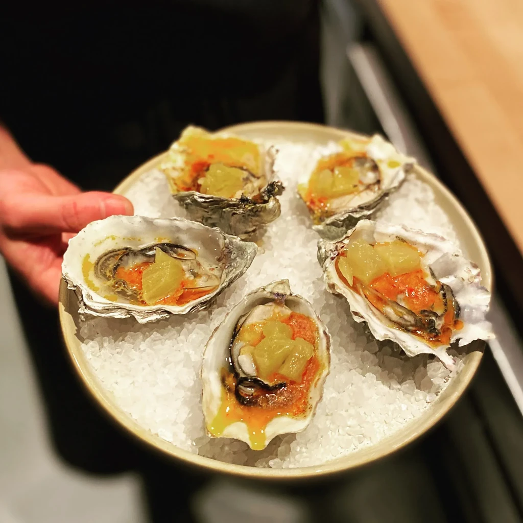 Five fresh oysters on half shell with sauce and fruit on ice.