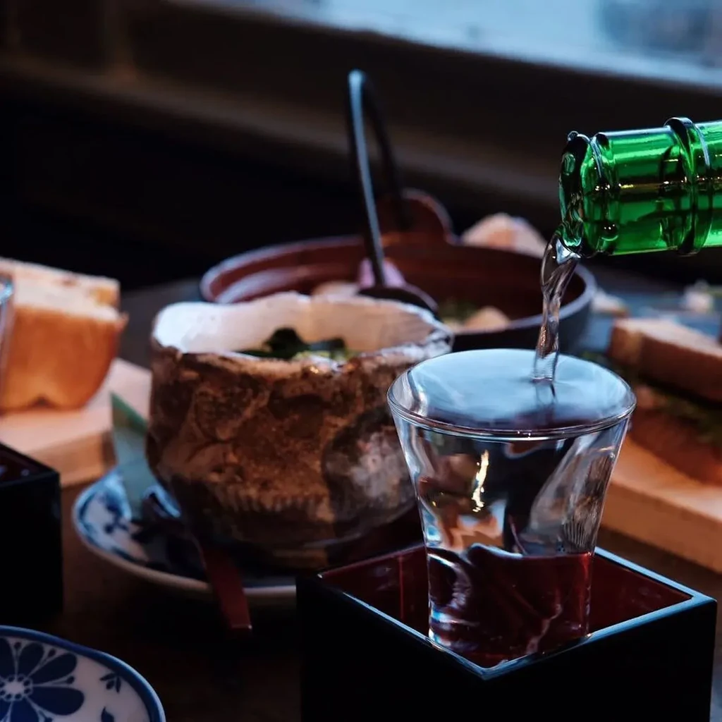 Green bottle pouring into a glass in a wooden masu cup.
