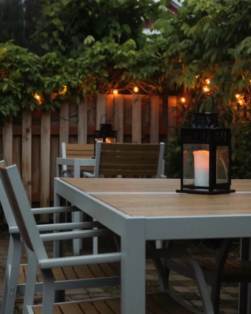 Outdoor dining patio with a lit lantern, string lights, and foliage.