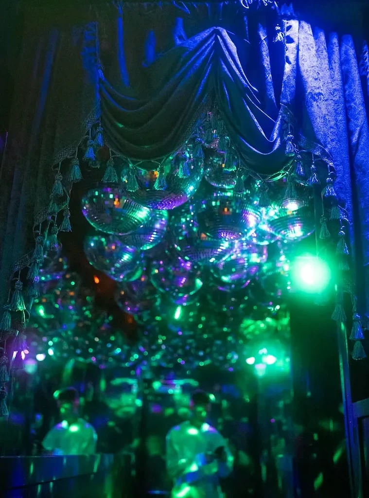 Disco balls reflect colorful lights under a blue draped curtain.