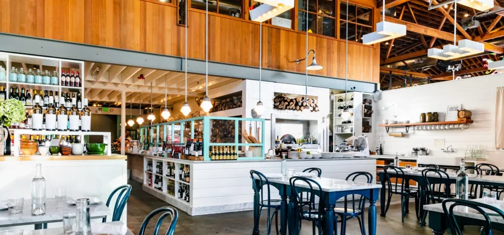 Bright modern-rustic restaurant interior with exposed wood beams and teal chairs.