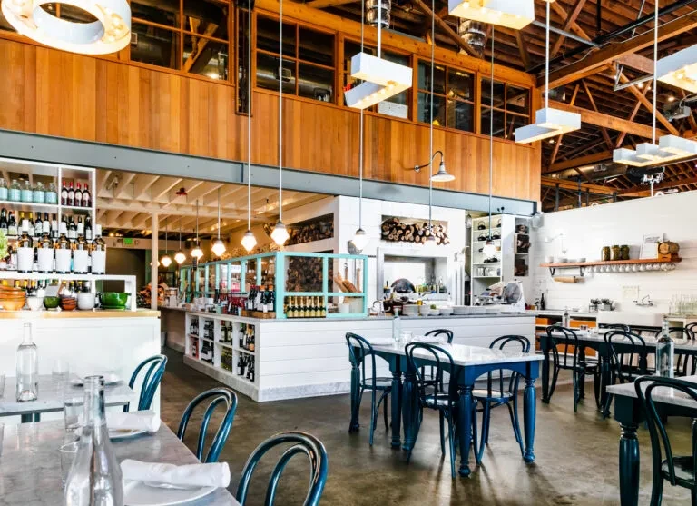 Spacious modern restaurant with wood beams, marble tables, and teal chairs.