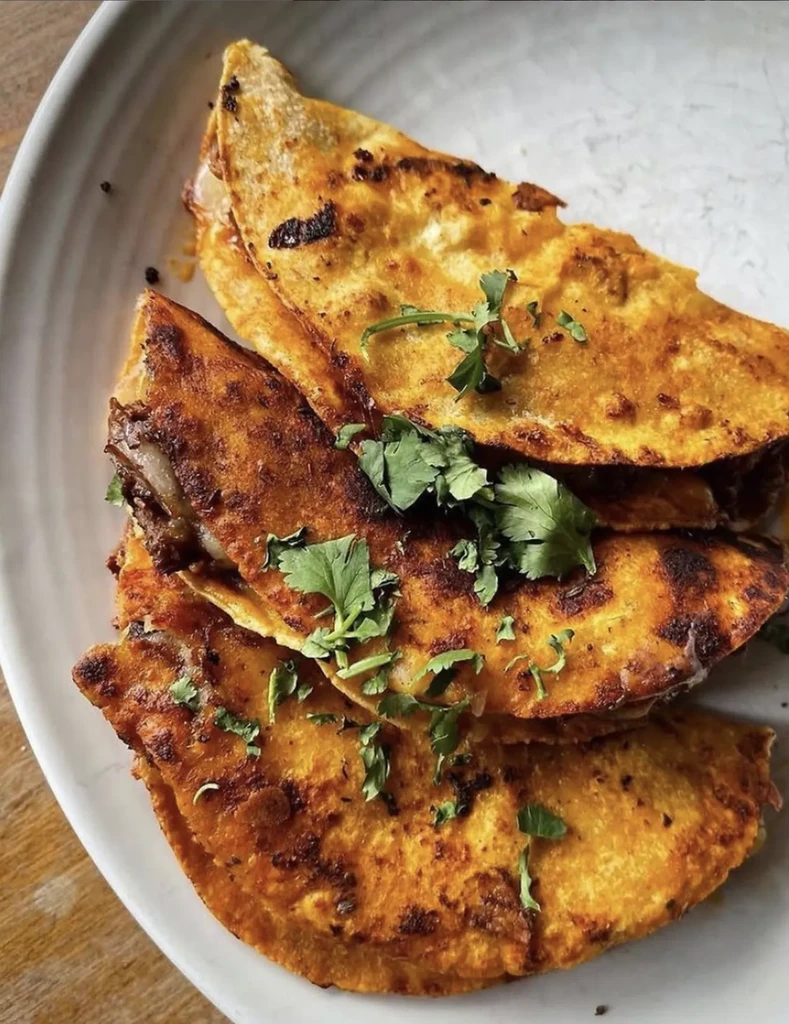 Three crispy quesabirria tacos with shredded meat and cilantro.