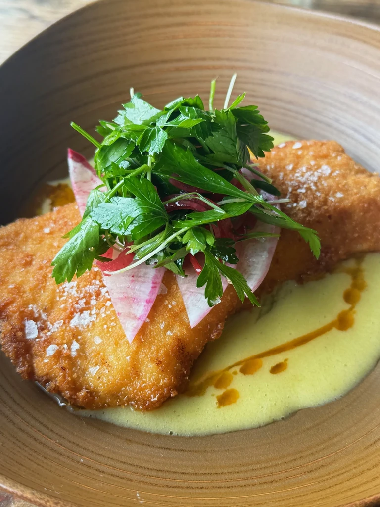 Plated golden-brown fried food with herbs, radish, and creamy sauce.