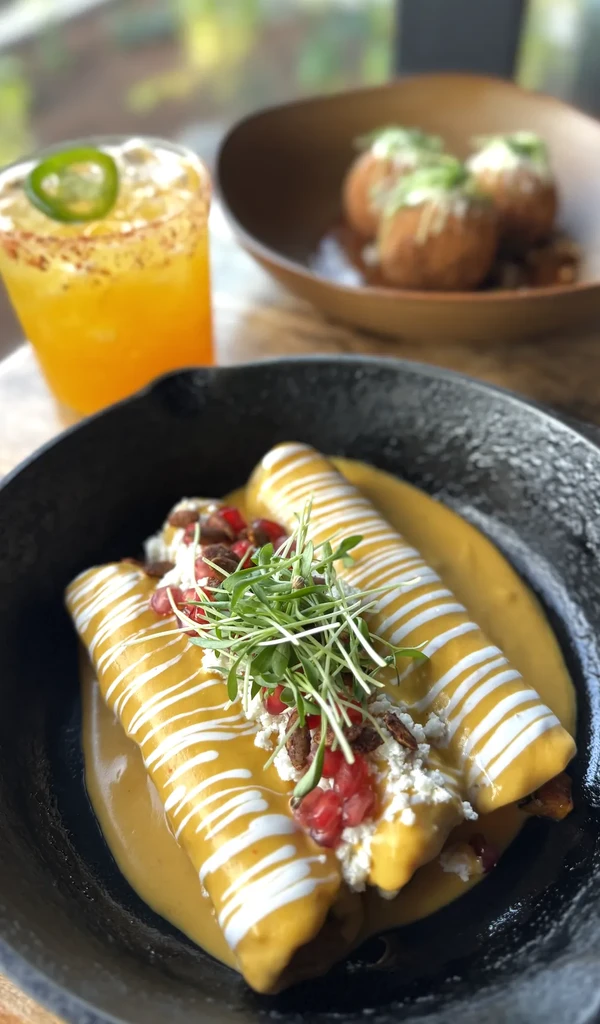 Artfully plated rolled food, microgreens, cheese, pomegranate, orange drink, fried items.