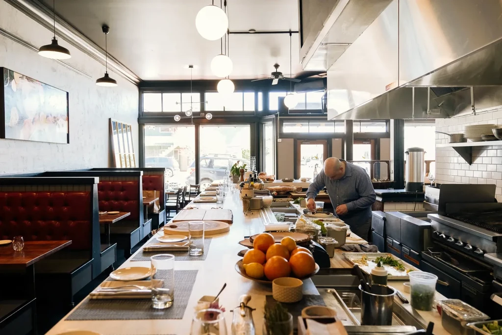 Modern restaurant with open kitchen, chef, dining counter, and red booths.