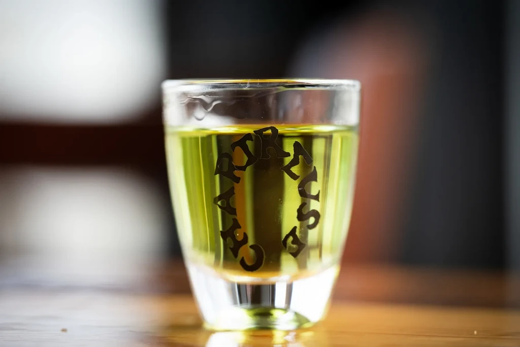Shot glass of yellow-green Chartreuse liquor on a wooden surface.
