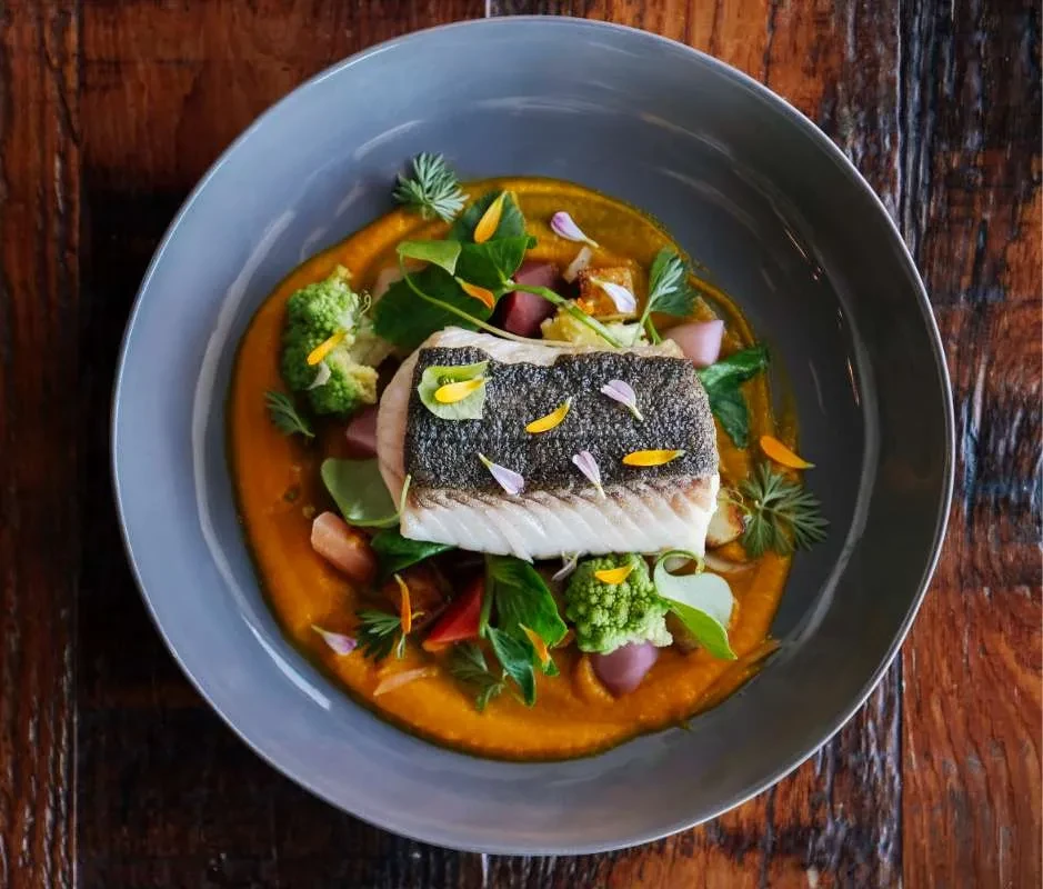 Pan-seared fish, purée, Romanesco, root vegetables, and edible flowers.