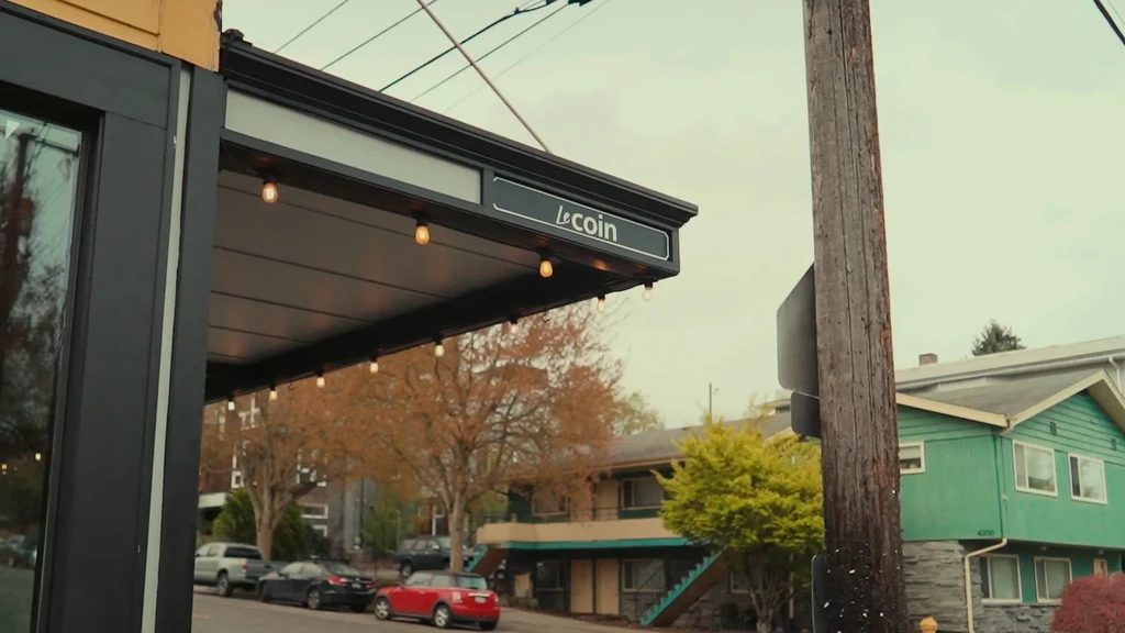 Muted street scene: Le Coin building with awning, string lights, cars.