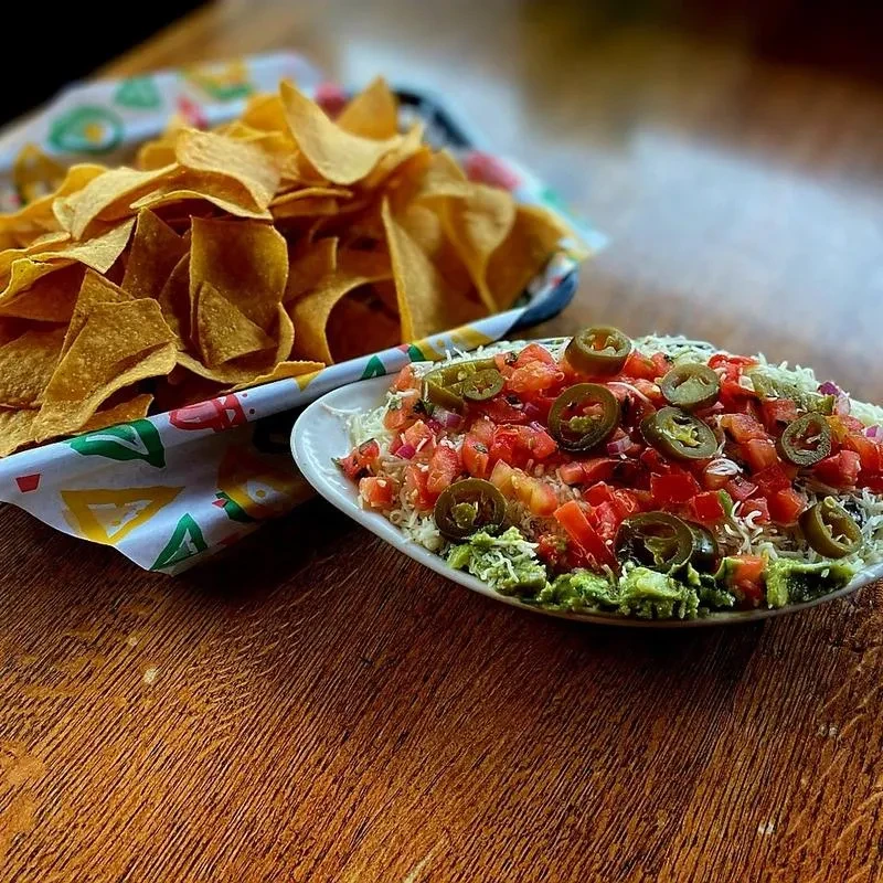Layered guacamole dip with pico de gallo, jalapeños, cheese, and chips.