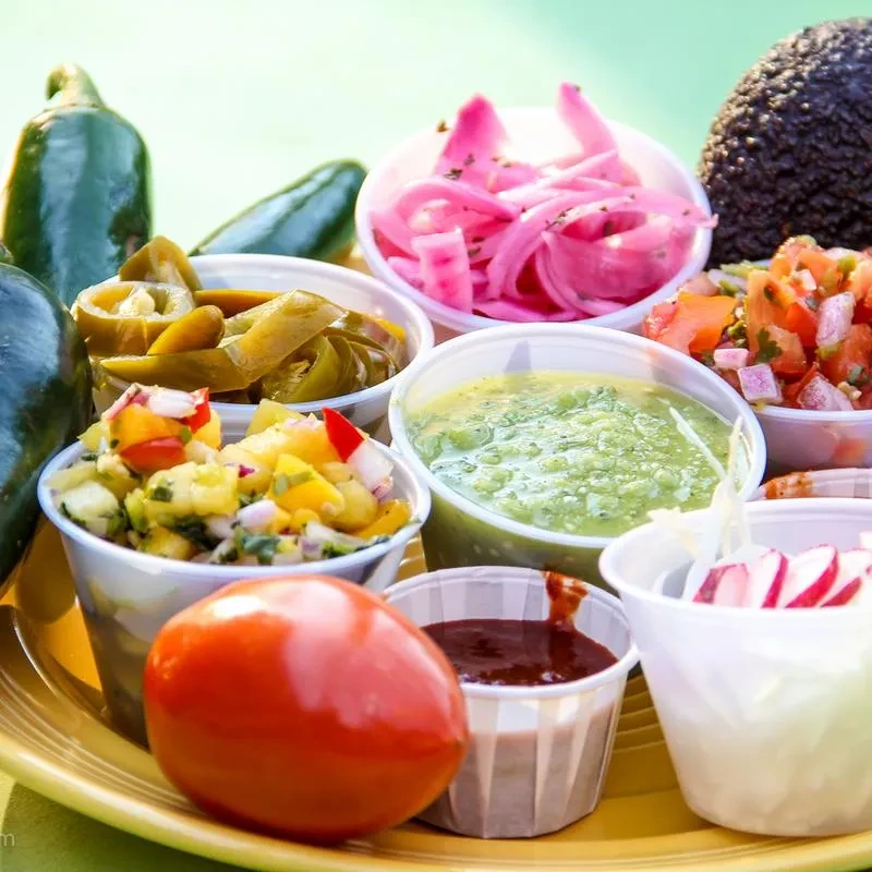 Mexican salsas, pickled vegetables, and fresh ingredients on a yellow plate.