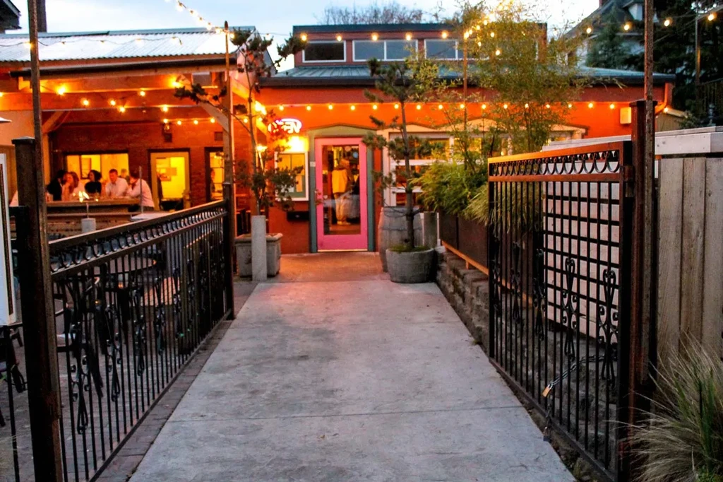 Evening reddish-orange restaurant, pink door, string lights, and patio guests.