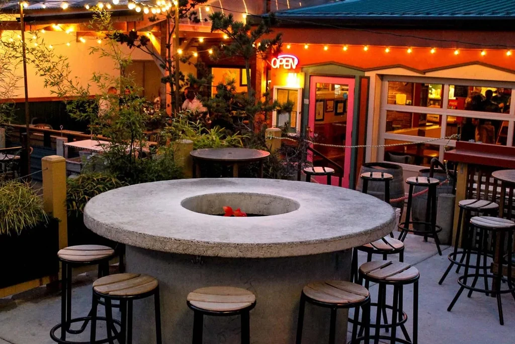 Evening patio with central fire pit table, string lights, and 'OPEN' sign.